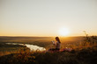 © eduard - Young woman reading book at sunset in front of beautiful landscape with fields and river.  Beautiful girl sitting on grass and reading a book.
