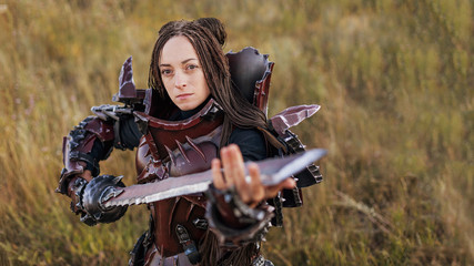 Wall Mural - Girl in medieval knight's armor with a big sword against the sunset fields background