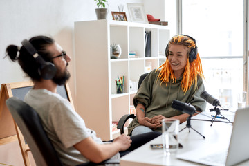 Two bloggers, young man and woman in headphones looking at each other while talking, recording conversation, interview for video blog