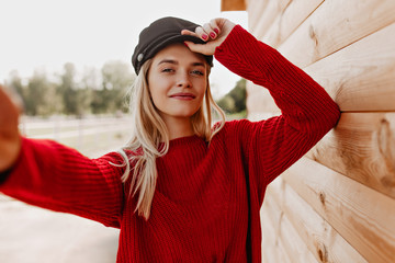 Wall Mural - Pretty blonde making selfie near the wooden. Attractive woman looking in the camera in treny red clothes.