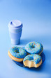 Served donuts with blue icing in a blue plate, with blue coffee mug next to it, isolated on top of blue background.