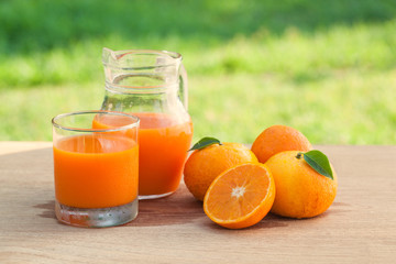 Canvas Print - Orange juice on a wooden table and jug with tree and field background