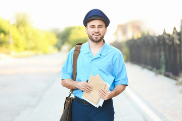 Wall Mural - Handsome young postman with letters outdoors