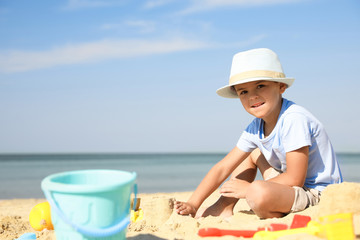 Poster - Cute little boy playing with plastic toys on sandy beach