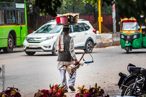 An old poor street snack food seller walks back home on a main road after a long day of hard work. Indian man carrying load on head to sell snacks on roadside. Poverty and daily wage earner labor.