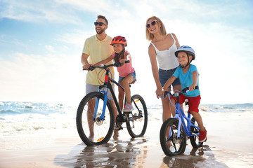 Sticker - Happy parents teaching children to ride bicycles on sandy beach near sea