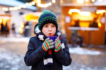 Wall Mural - Little cute kid boy drinking hot children punch or chocolate on German Christmas market. Happy child on traditional family market in Germany, Laughing boy in colorful winter clothes