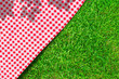 Red checkered table cloth on green turf or grass from top view.
