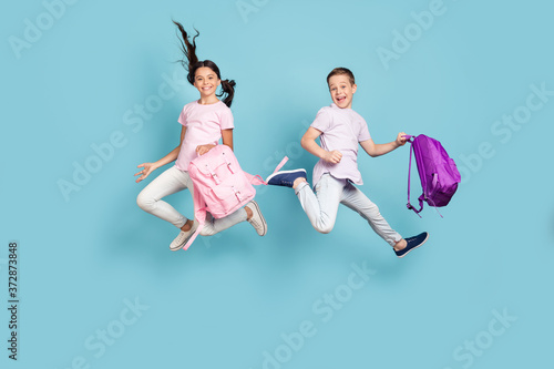 Full length body size view of his he her she nice attractive small little cheerful best buddy fellow jumping having fun after classes fooling leisure free time isolated blue pastel color background