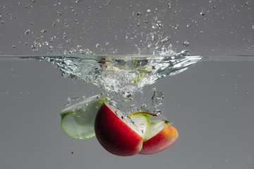 Red and green apple slices fall into water and create beautiful air bubbles and water splashes