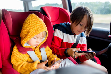 Wall Mural - Three children, boys, traveling in car in carseat and playing on mobiles