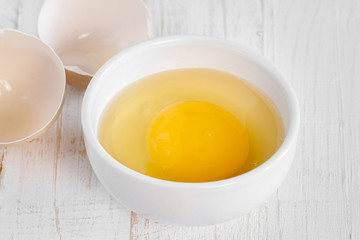 Row fresh egg in ceramic small white plate and two parts of shell on painted wooden background macro