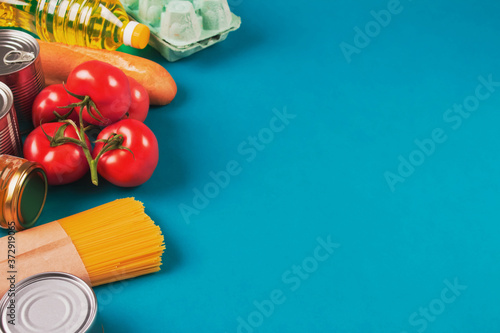 Top view on food donations on green background with copyspace - pasta, fresh vegatables, canned food, baguette, eggs, organic oil. Donation, volunteering or contactless delivery food concept. Flat lay