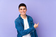 Teenager caucasian  handsome man isolated on purple background pointing back