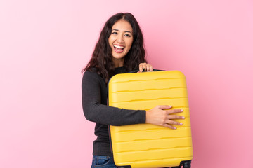 Wall Mural - Mixed race woman over isolated pink background in vacation with travel suitcase