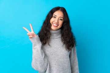 Wall Mural - Spanish Chinese woman over isolated blue background smiling and showing victory sign