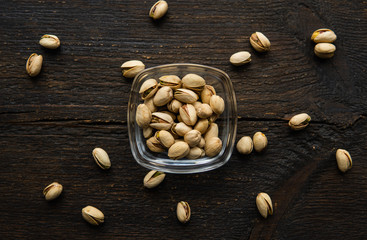 Wall Mural - Pistachios in a small plate with scattered nuts of almonds around a plate on a vintage wooden table as a background. Pistachio is a healthy vegetarian protein nutritious food. Natural nuts snacks.