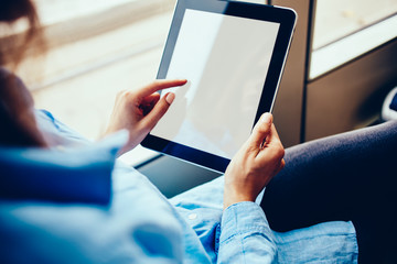 Cropped view of woman's hands holding modern touch pad device and touching on blank screen area sitting in tram and using free public internet connection for chatting online in social networks