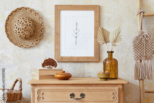 Photographie Stylish boho interior of living room with brown mock up poster frame, elegant accessories, flowers in vase, wooden shelf and hanging rattan hut