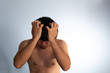 © Antonio Tanaka - Young naked Hispanic man with wavy hair and shaved beard on a white background, covering his face with his hands tightly