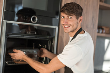 smiling young man warming up dinner in his kitchen