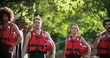 four friends wearing life vests walking to river to start rafting river descent. People wearing life jackets walking to camera. Rafting adventure sport.