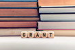 © Cagkan - The word grant on wooden cubes with stacked books background. Education or research funding concept.
