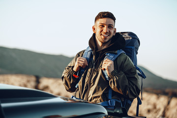 portrait of a young traveler man in hiking equipment standing near his off-road car