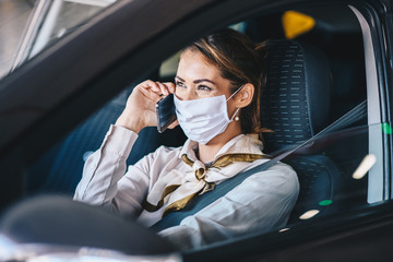 A young woman sits in a car with a mask on her face and talks on a mobile phone, life during a virus pandemic