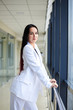 © Natalia - Young brunette woman, wearing white pants and jacket, standing in light passageway with huge windows, posing for social media, leaning on railing. Businesswoman on a break. Female portrait photography