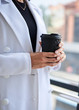 © Natalia - Close-up picture of black paper coffee cup, held n hands of young woman, Businesswoman on lunch break, standing by window. Corporate culture concept.