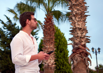 Sticker - Closeup shot of male model holding a phone and posing on background of palms