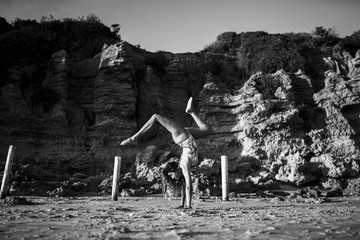 Poster - Grayscale shot of a beautiful female in a swimsuit doing a trick on sands