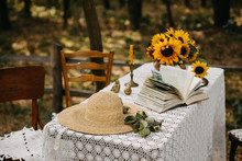 Decorated Table With Crochet Tablecloth, Sunflowers And A Straw Hat In A Park.