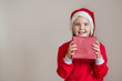 Happy girl in santa costume with gift on light gray background 
