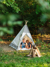 Two Young Boys Playing In A Backyard Teepee Campsite Under The Summer Sunset