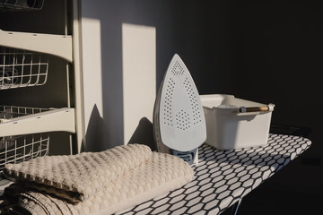 Electric iron and pile of towels on ironing board in laundry room at home