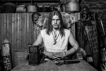 A brutal male in traditional Russian clothes sits on a wooden throne at a dining table