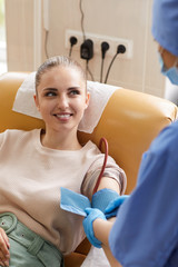 Young woman lying on couch and donating blood while smiling to nurse