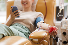 Close-up Of Young Woman Lying On The Couch With Mobile Phone While Donating Blood At The Laboratory