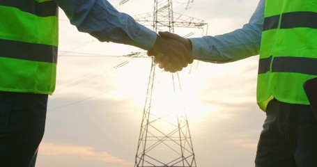 Wall Mural - close up of a handshake of two men in orange signal vests against the background of the sun and an i