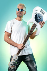 Confident hipster man posing with white bass guitar in neon lights. Rock music concept. Rock star.