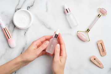 Wall Mural - female hand holding serum bottle over marble table with moisturizer cream, makeup brush, face massag