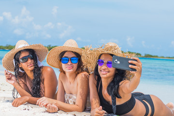 Wall Mural - three multi ethnic women friends lying back taking selfie with sunlight at blue water beach