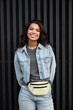 Smiling pretty cheerful African American teen hipster girl looking at camera standing on black background, vertical. Happy positive mixed race young woman wearing denim jacket posing for portrait.