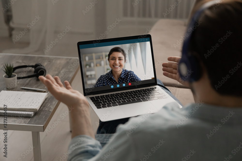 Over shoulder view of man speak talk on video call on laptop with smiling ethnic woman wife, male have webcam virtual digital conference or online business meeting with colleague at home office - obrazy, fototapety, plakaty 