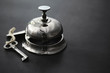 © alexkich - A shiny silver metal bell at the hotel reception. A table in the hotel at the concierge with a bell and a door key. Key and bell in a hotel.