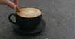 adding cinnamon stick into cappuccino in black cup on terrazzo countertop