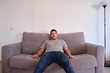 © Ladanifer - Portrait of a bored and tired young man sitting on a sofa watching television absorbed with his mouth opened.