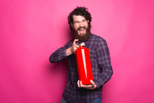 Photo Of Young Bearded Man In Shirt Holding Fire Extinguisher Over Pink Background.